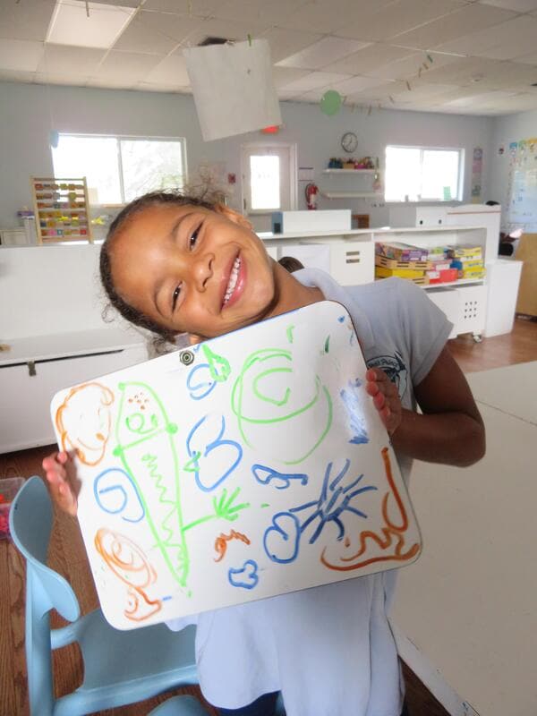 A smiling student holding up a marker drawing