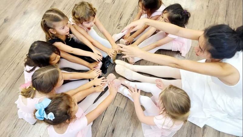 Ballet students stretching in a circle with their teacher