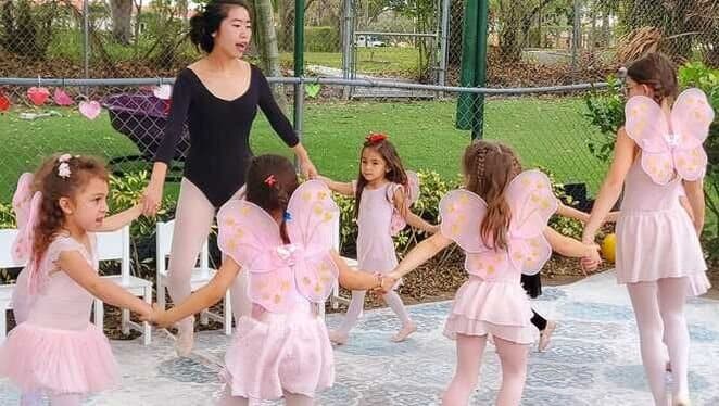 Students in tutus dancing in a circle with their ballet teacher