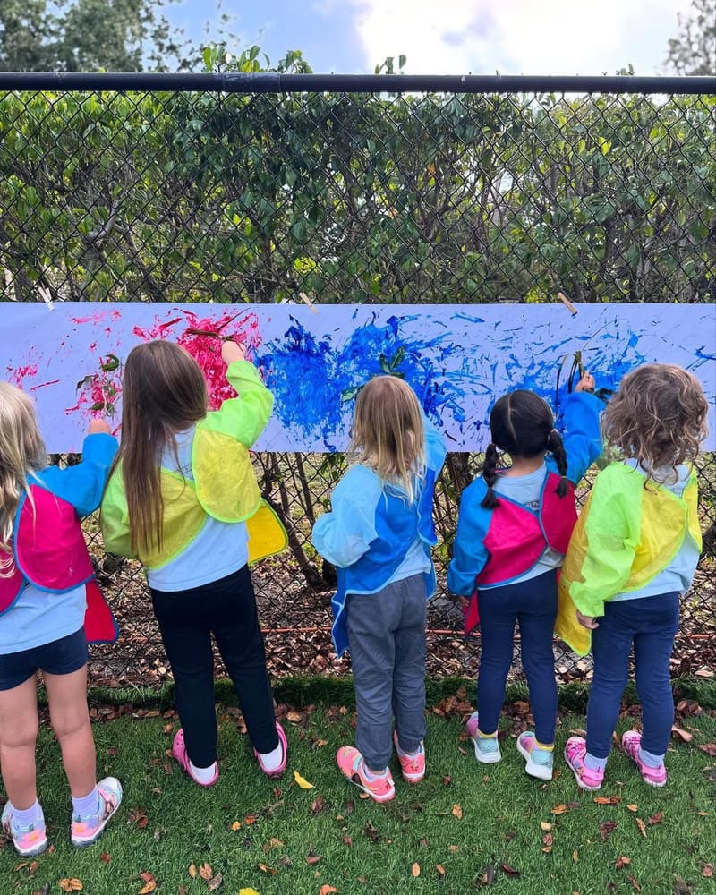Students painting a long mural on the playground fence