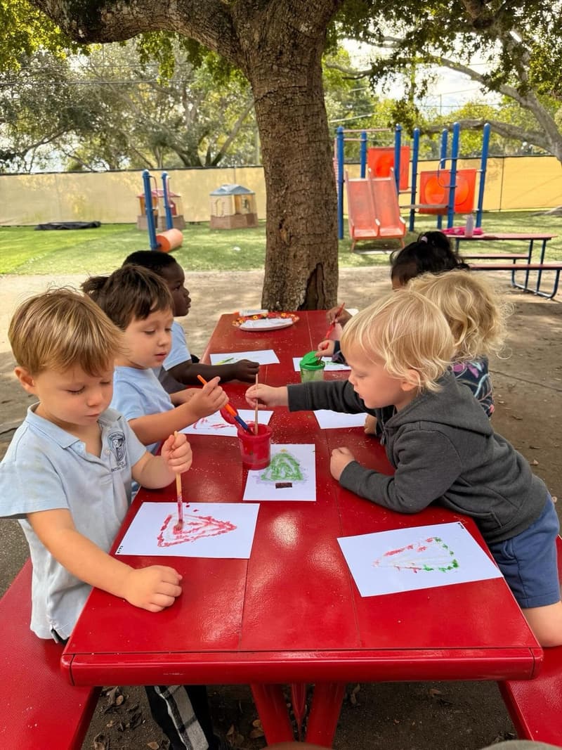 Students painting at the picnic tables under the tree