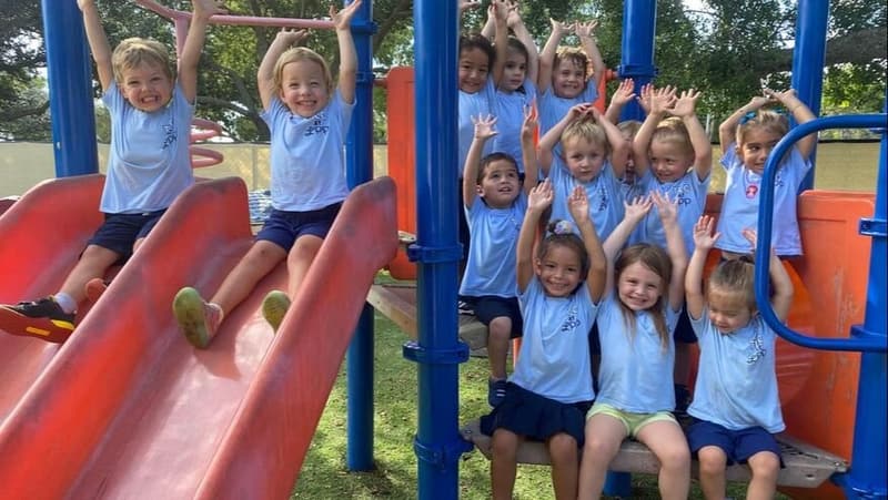 A class cheering with hands up on the playground slide