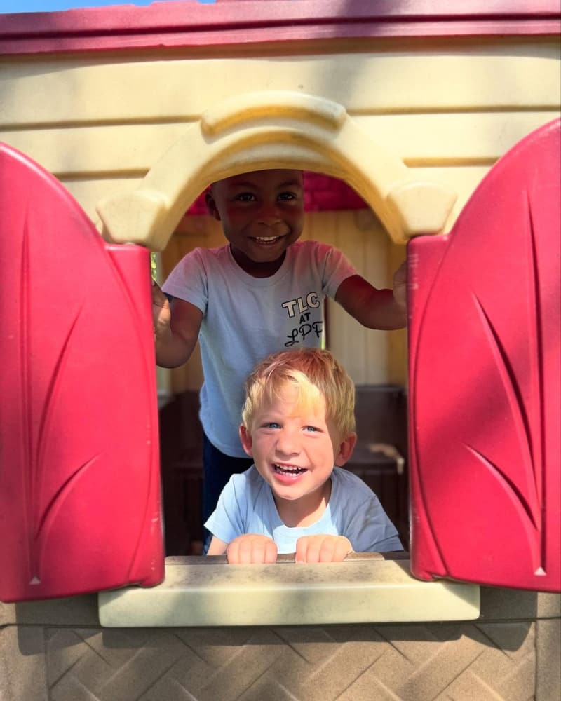 Two students peeking out of a playhouse window