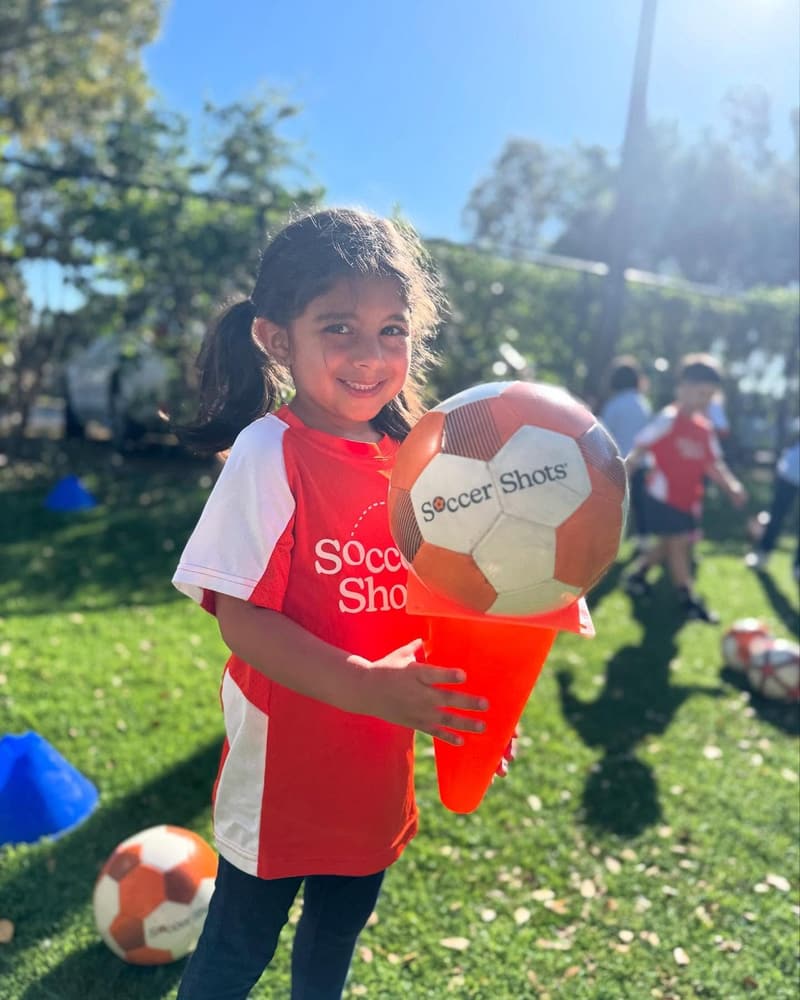 A student in a Soccer Shots jersey holding a soccer ball