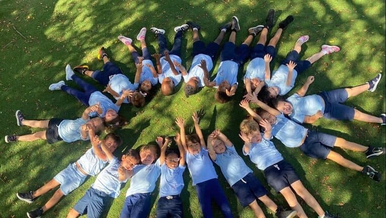 Students lying on the grass in a circle, heads together