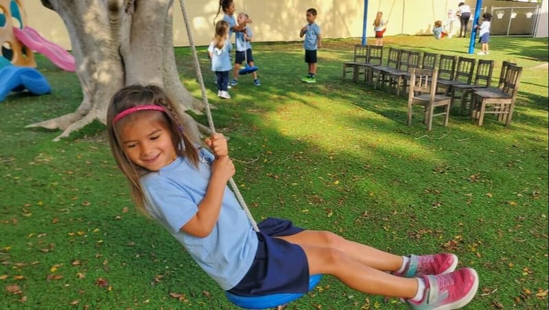 A student on a rope swing under the big shade tree on the playground