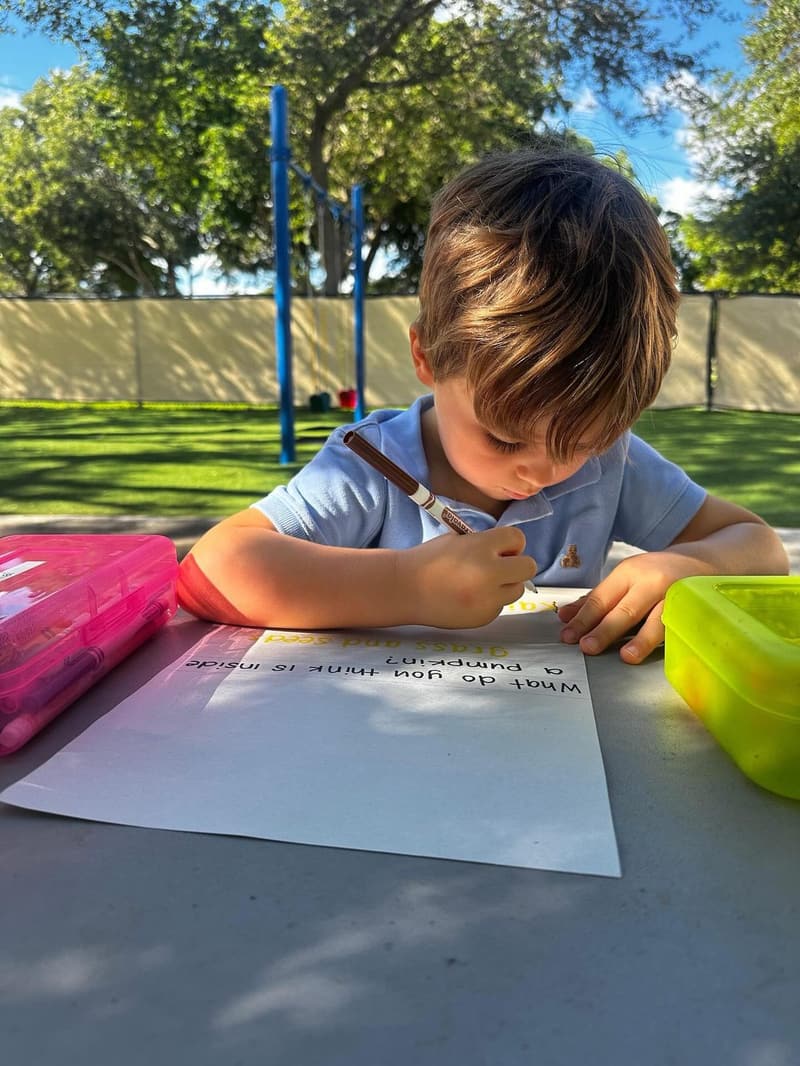 A student writing at a table outdoors